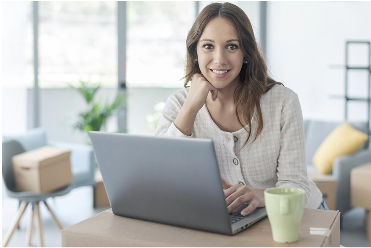 A woman in front of her laptop with moving boxes researching moving tips
