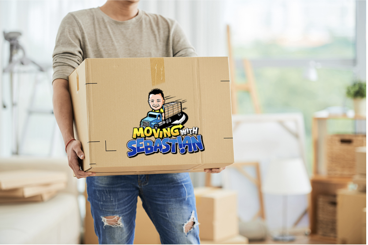 A man in jeans and t shirt carrying a large cardboard box with a logo on it from Moving With Sebsatian on moving day in his Boca Raton condo